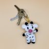 Handmade crochet cow keychain on a soft pastel backdrop with a set of keys