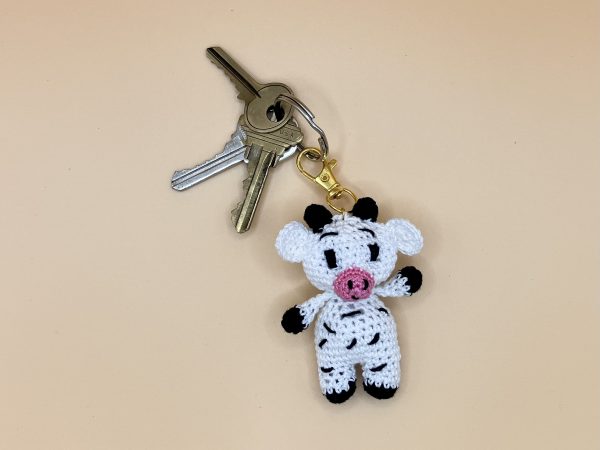 Handmade crochet cow keychain on a soft pastel backdrop with a set of keys