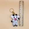 Handmade cow keychain next to a wooden ruler for size reference.