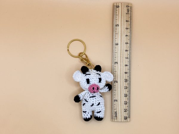 Handmade cow keychain next to a wooden ruler for size reference.