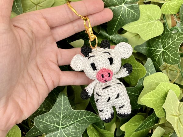 Handmade crochet cow keychain displayed against a lush plant backdrop, crafted with black and white cotton yarn, perfect for nature-inspired accessories