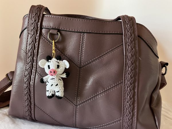 Handmade crochet cow purse charm attached to a purple purse, featuring black and white cotton yarn, perfect for adding a cute accessory to everyday bags.