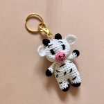 Handmade crochet cow keychain on soft pink backdrop, featuring black and white cotton yarn, ideal for animal-themed accessories.