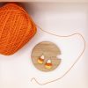 Candy corn earrings laying on a wood coaster next to a ball of orange yarn