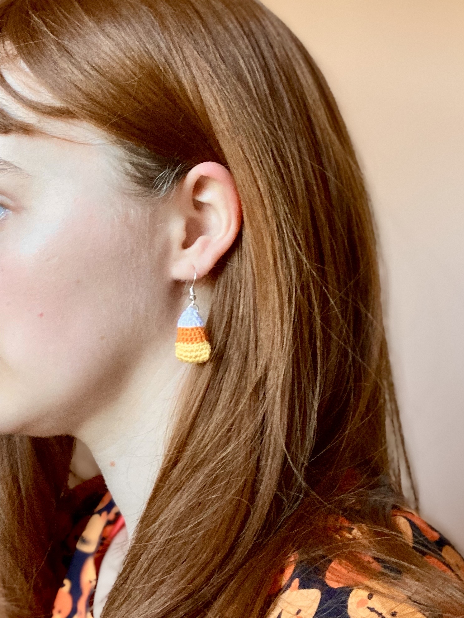 A reference image of a model wearing a crochet candy corn earring