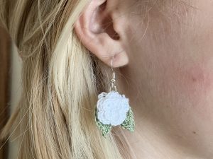 A reference image of a model wearing white crochet rose earrings