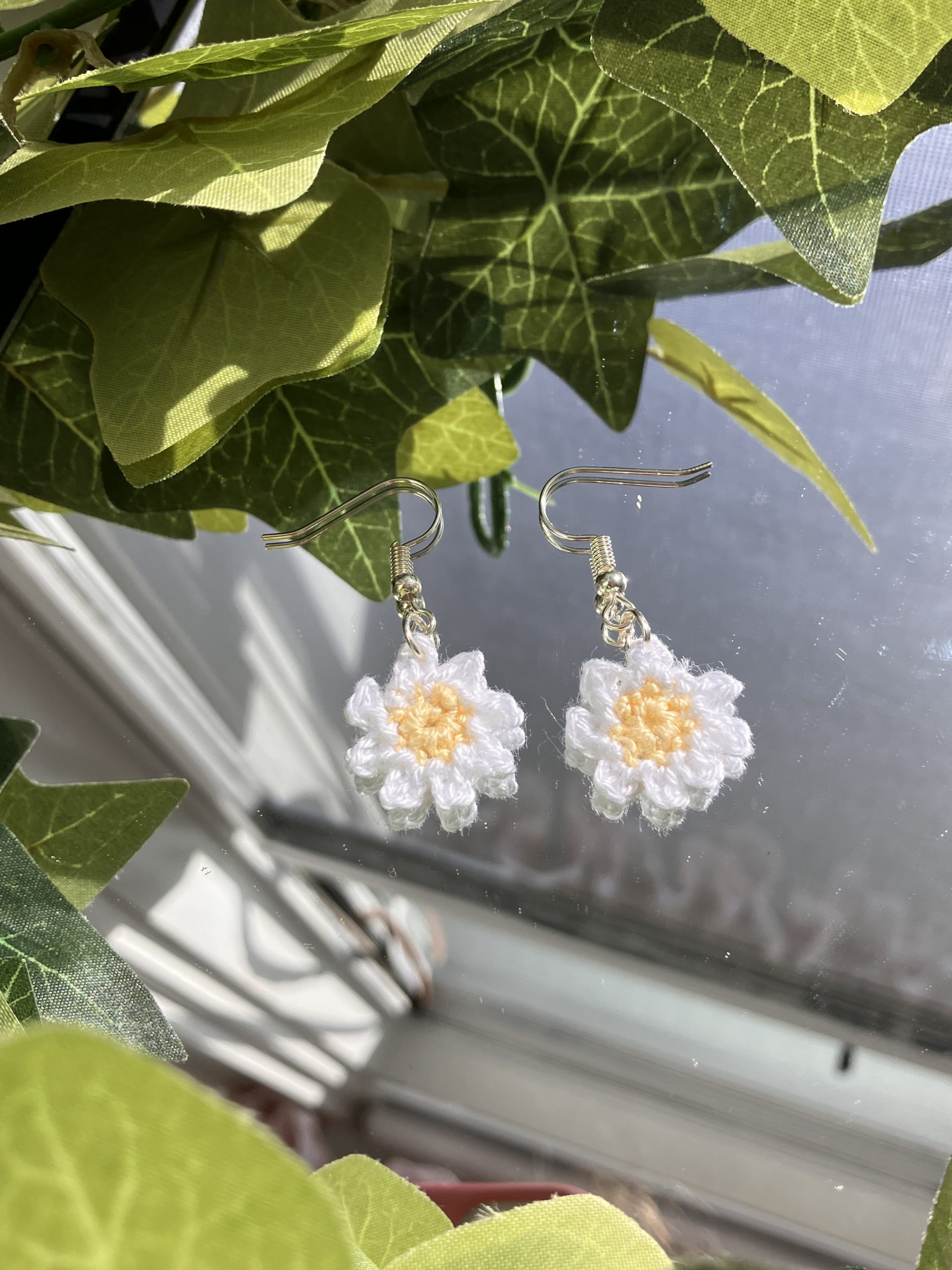 Crochet daisy earrings laying on a mirror