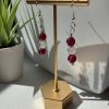 Burgundy and white beaded dangle earrings hanging on a gold earring stand