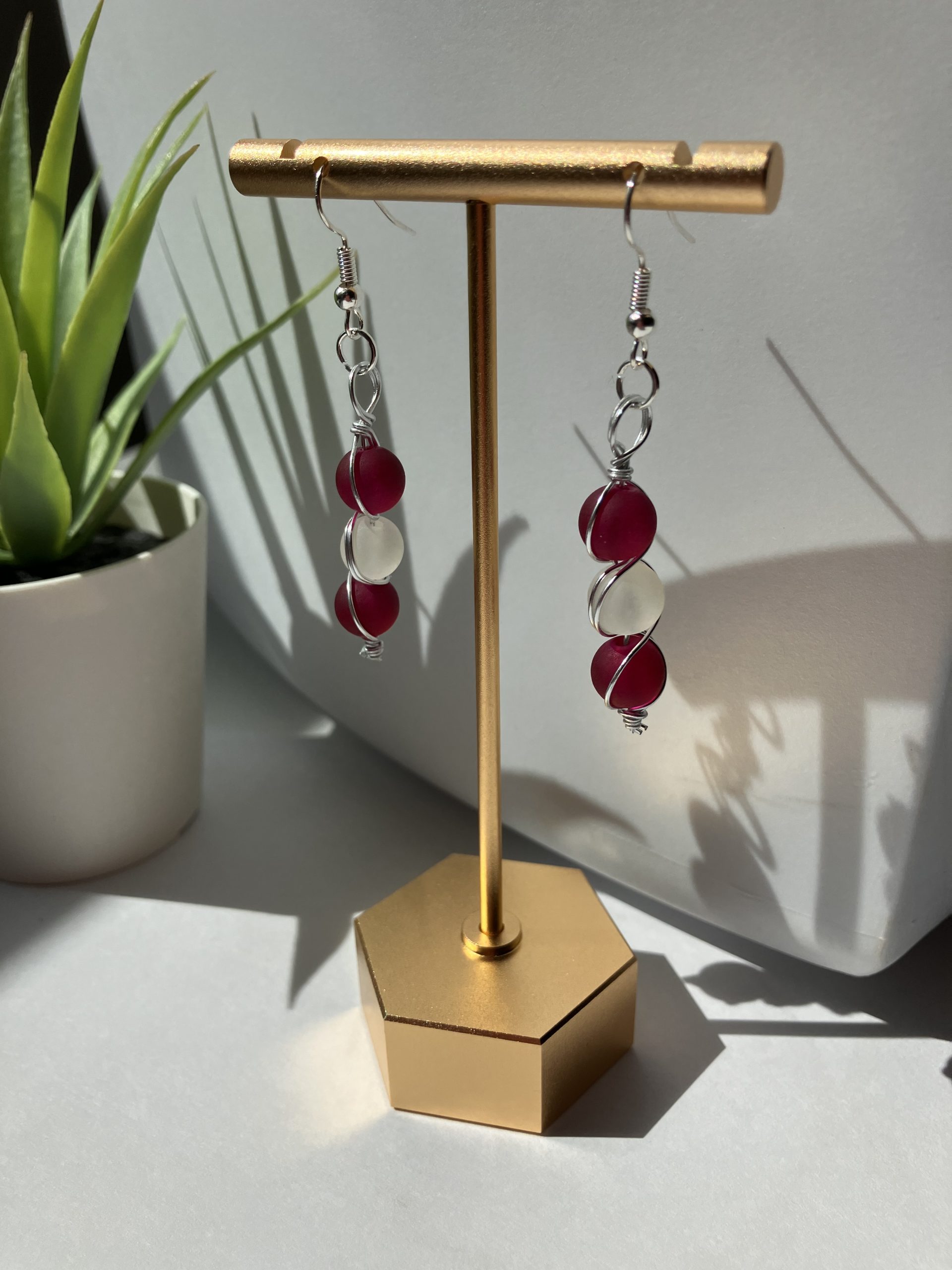 Burgundy and white beaded dangle earrings hanging on a gold earring stand