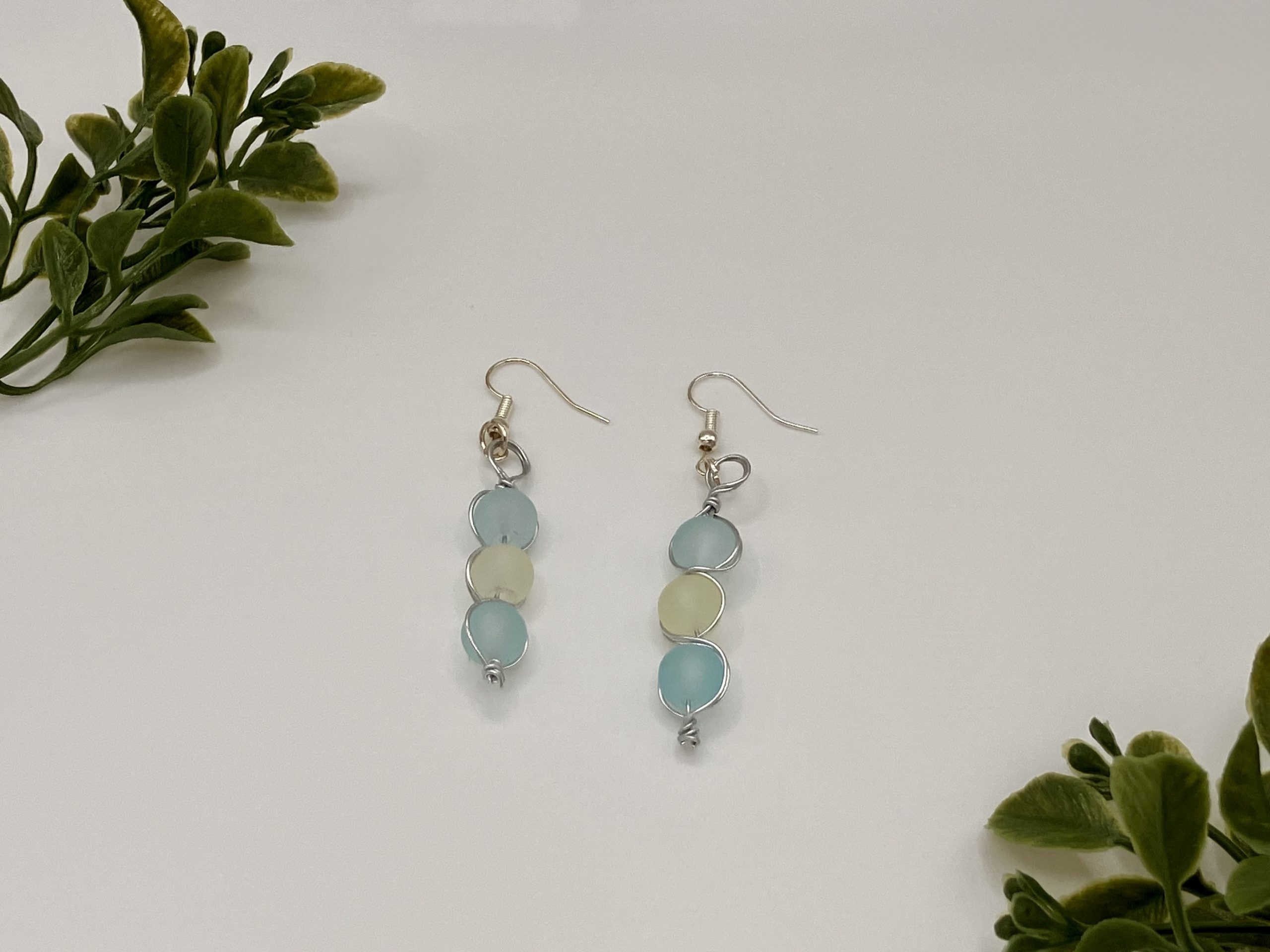 Sea blue and white beaded dangle earrings laying flat on a white Backdrop