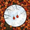 Handmade crochet pumpkin earrings, laying flat on a mirror surrounded by fall leaves