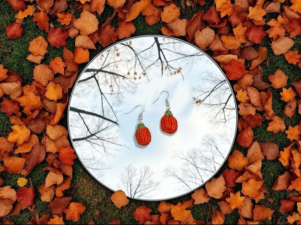 Handmade crochet pumpkin earrings, laying flat on a mirror surrounded by fall leaves