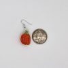 Crochet pumpkin earring next to a quarter for size reference