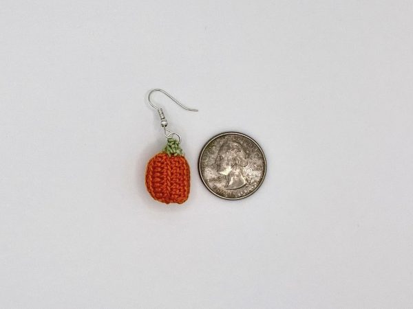 Crochet pumpkin earring next to a quarter for size reference