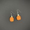 Crochet pumpkin earrings laying flat on a black surface