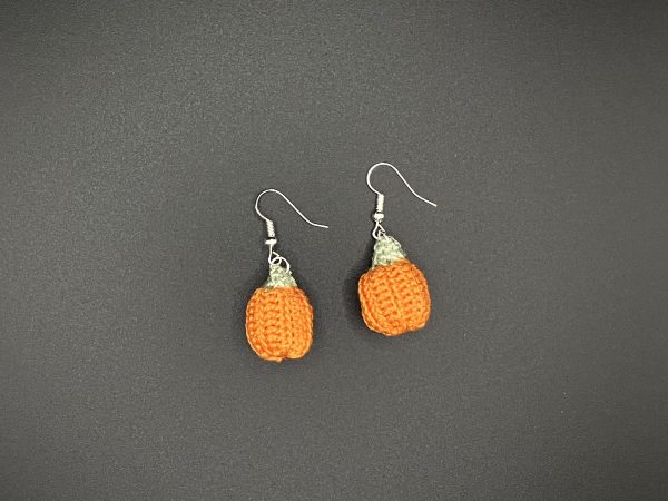 Crochet pumpkin earrings laying flat on a black surface