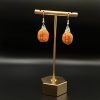 Crochet pumpkin earrings hanging on a gold earrings display stand