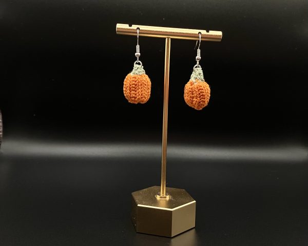 Crochet pumpkin earrings hanging on a gold earrings display stand