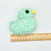 Green crochet duck plushie next to a ruler for size reference
