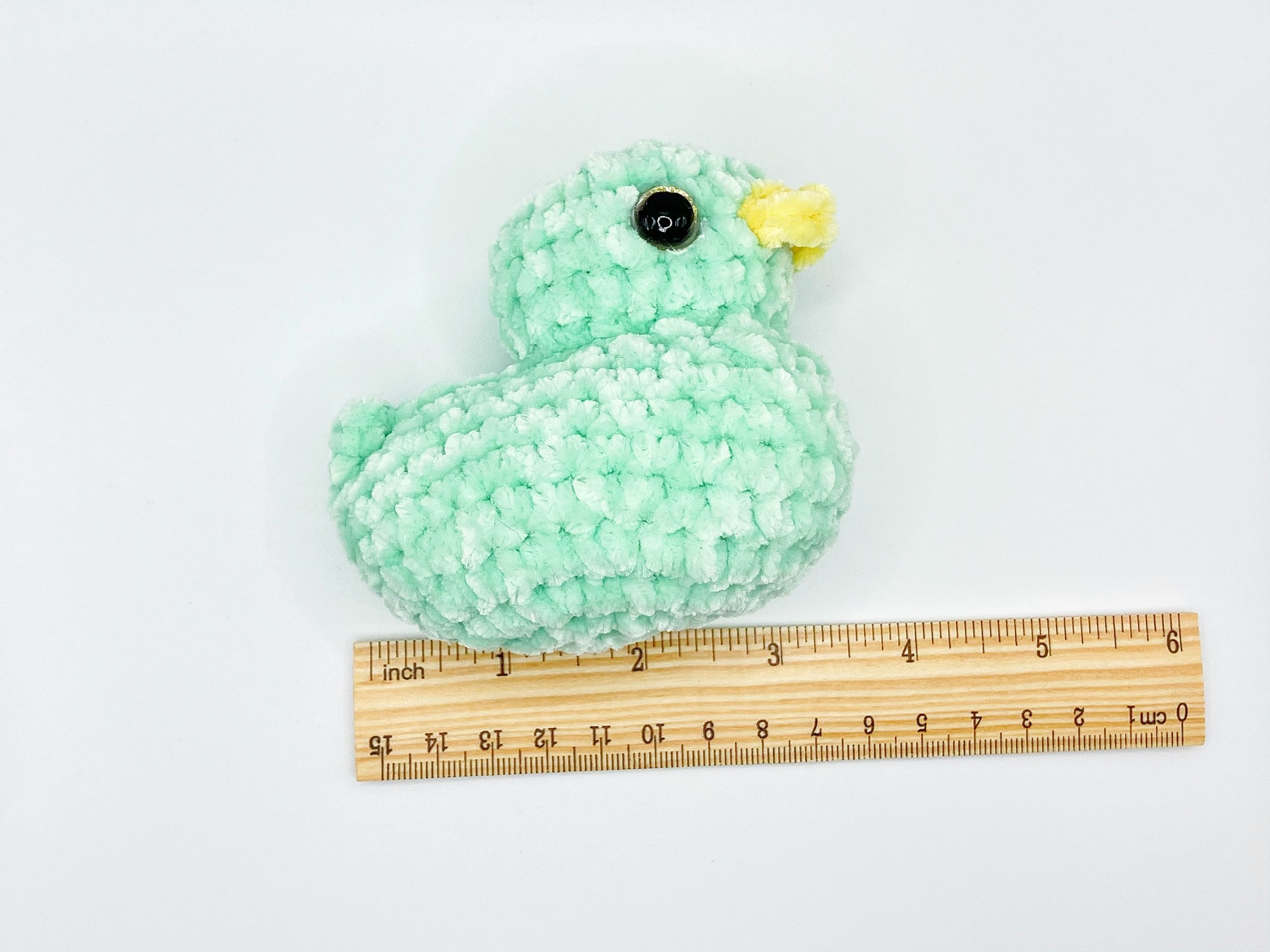 Green crochet duck plushie next to a ruler for size reference