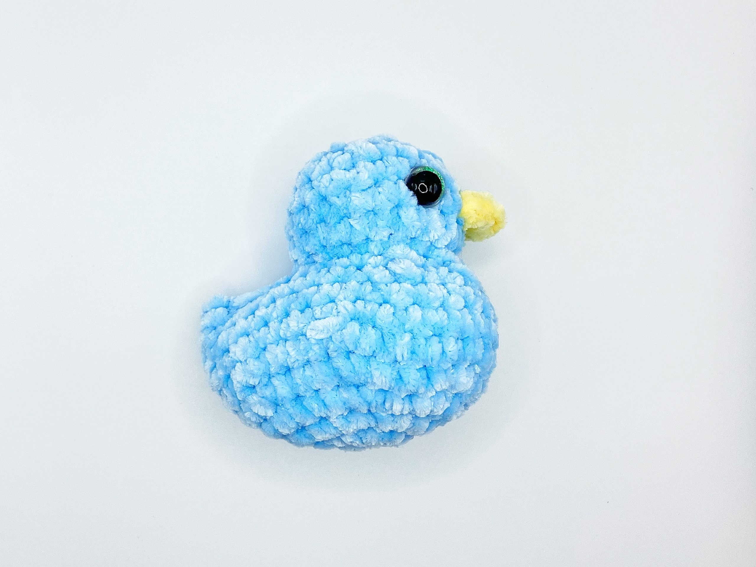Blue crochet duck plushie laying on its side
