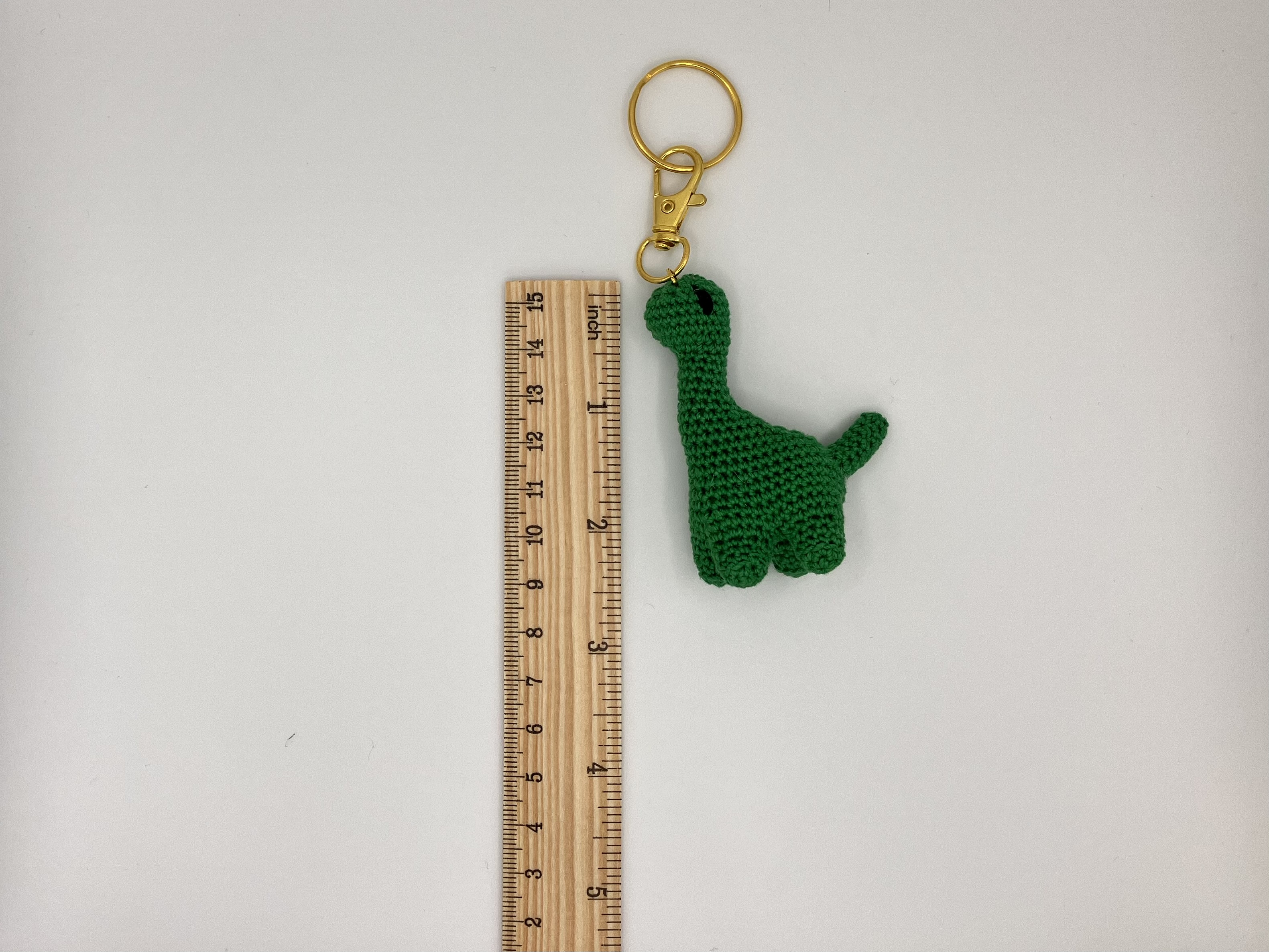 Green crochet dinosaur keychain next to a ruler for size reference