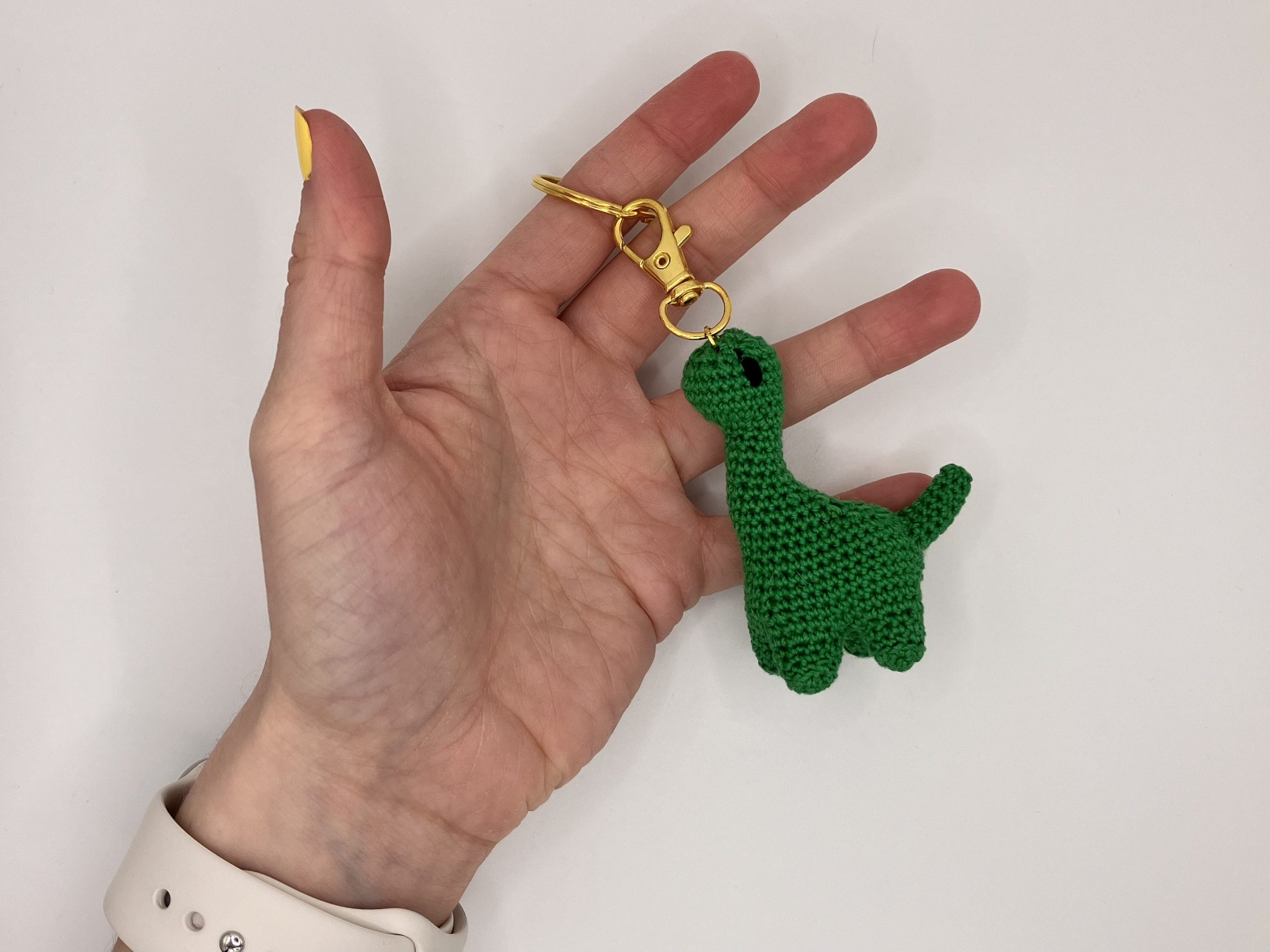 Green crochet Dinosaur keychain in a hand for size reference
