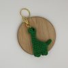 Green dinosaur crochet keychain charm laying flat on a wood coaster