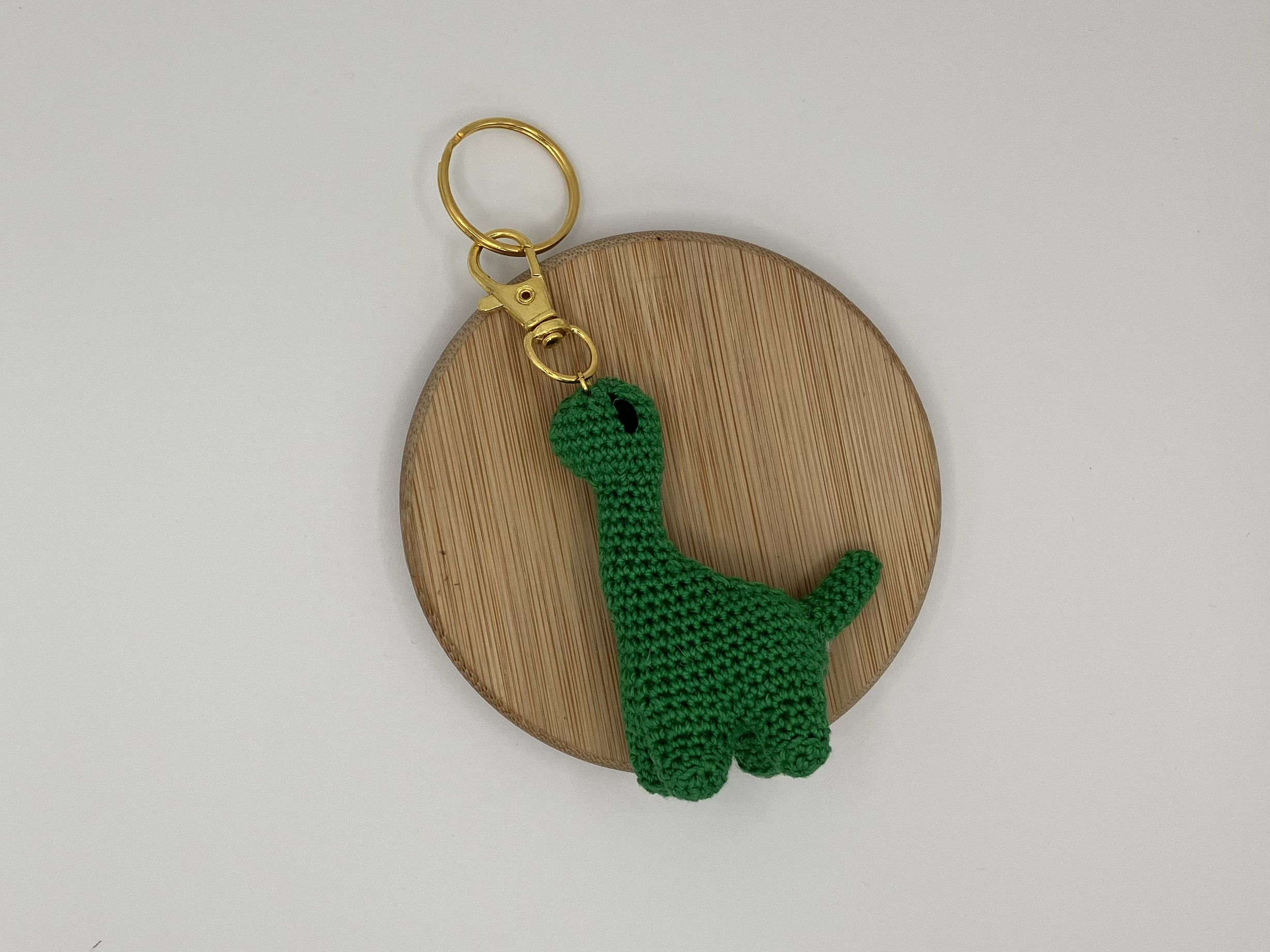 Green dinosaur crochet keychain charm laying flat on a wood coaster